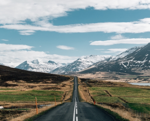 Road surrounded by hills covered in greenery and snow under a cloudy sky in Iceland
